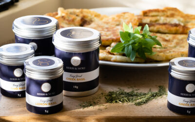 Multiple dark blue and silver tins of freeze-dried herbs on wooden board with flatbread in background