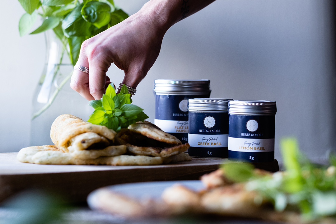 Lady placing herbs on top of yoghurt flatbreads with blue and silver tins of herbs next to it