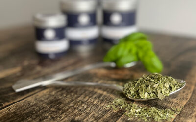 Freeze-dried basil on spoon with tins and basil leaves in background